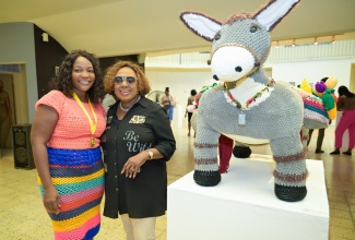 Minister of Culture, Gender, Entertainment and Sport, Hon. Olivia Grange (right), shares a photo moment with St. Mary crotchet artist Glenevea Paul-Penny (left), who won gold in the 2025 Jamaica Cultural Development Commission (JCDC) Visual Arts Competition. Beside them is a display of her crotchet piece titled ‘Jah Kass Seh Di World Nuh Level’.

