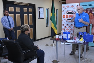 State Minister in the Ministry of Health and Wellness, Hon. Krystal Lee (centre), observes as Founder and Chief Executive Officer of WaterStep, Mark Hogg, demonstrates how the water-purification bleach makers function during the handover ceremony for 300 machines at the Office of Disaster Preparedness and Emergency Management (ODPEM) in New Kingston on Tuesday (November 18). Also looking on is the Ministry’s Director of Communication, Stephen Davidson (left). The durable systems enable health facilities to produce World Health Organization (WHO)-approved, medical-grade disinfectant on site, ensuring a stable local supply while expanding access to safe water and sanitation solutions, particularly during disasters.
