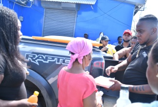 Members from the Pure Ultra Lounge team (right), distribute meals and care packages to Fustic Road residents in St. James on Sunday (November 9). 