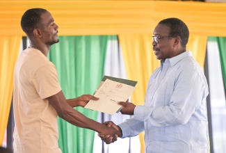 Minister without Portfolio in the Ministry of Economic Growth and Infrastructure Development with responsibility for Land Titling and Settlements, Hon. Robert Montague (right), hands a St. Elizabeth resident his land title, during a ceremony held at the Lacovia Community Centre in the parish on Friday (December 12).

