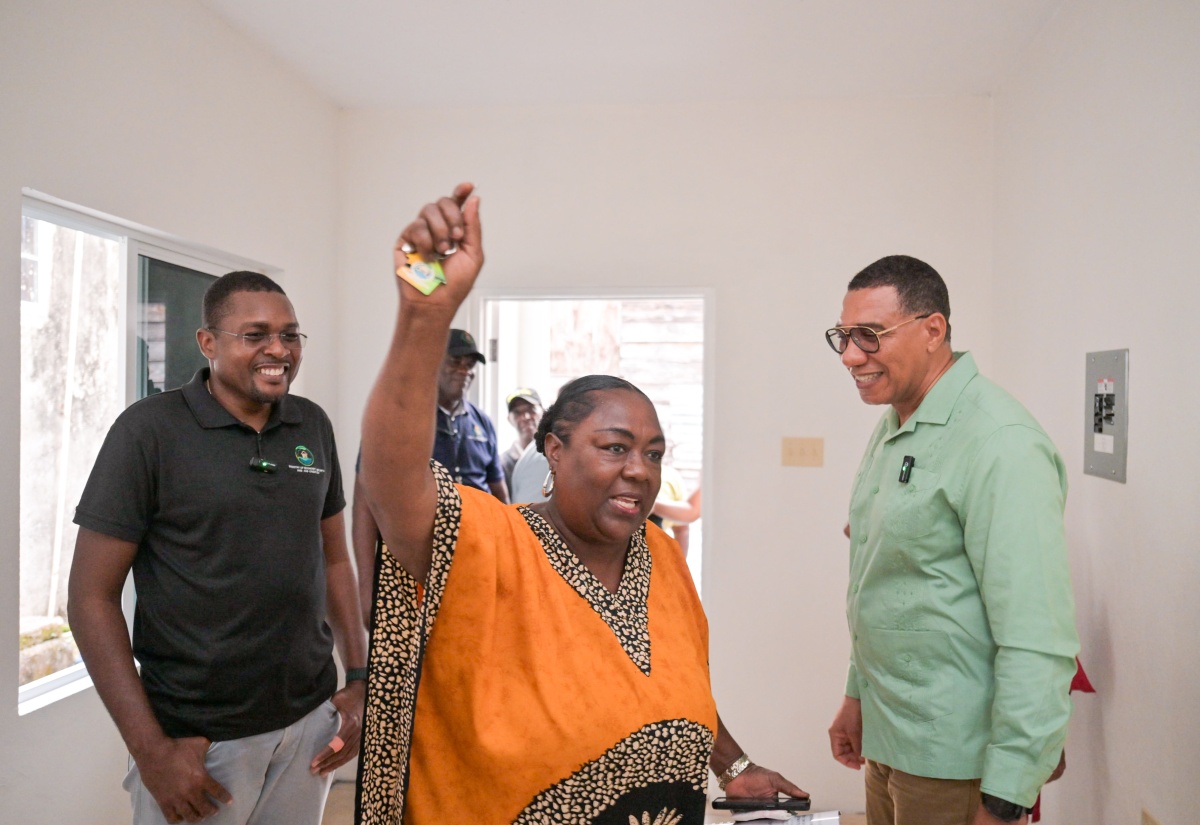 Prime Minister, Dr. the Most Hon. Andrew Holness (right), and Minister without Portfolio in the Ministry of Economic Growth and Infrastructure Development with responsibility for Works and Member of Parliament for Clarendon North Central, Hon. Robert Nesta Morgan, smile as New Social Housing Programme (NSHP) recipient Angella Boothe raises the key to her new two-bedroom house in Mocho, Clarendon. The unit was handed over by the Prime Minister on Friday (December 19). 

