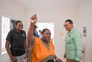 Prime Minister, Dr. the Most Hon. Andrew Holness (right), and Minister without Portfolio in the Ministry of Economic Growth and Infrastructure Development with responsibility for Works and Member of Parliament for Clarendon North Central, Hon. Robert Nesta Morgan, smile as New Social Housing Programme (NSHP) recipient Angella Boothe raises the key to her new two-bedroom house in Mocho, Clarendon. The unit was handed over by the Prime Minister on Friday (December 19).