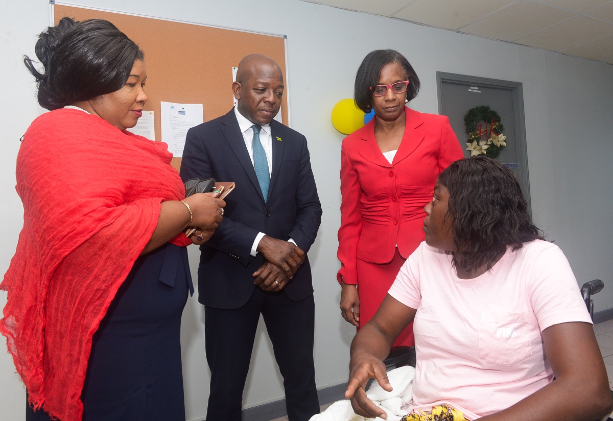 Minister of Labour and Social Security, Hon. Pearnel Charles Jr. (centre), engages in discussion with beneficiary, Darnett Denton (seated), during Tuesday’s (December 16) Assistive Aid Grant and Margaret Moody Scholarship Handover Ceremony at the Jamaica Council for Persons with Disabilities (JCPD) in Kingston. Joining them are Acting Executive Director, JCPD, Desreen Boothe (left), and Acting Permanent Secretary in the Ministry of Labour and Social Security, Dione Jennings.

