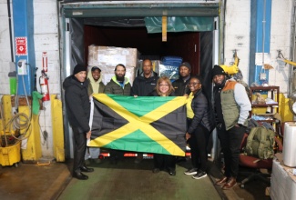 Jamaica’s Ambassador to the United States, His Excellency Major General (ret’d) Antony Anderson (left), President and Chief Executive Officer of EMD Sales International, Elda Devaré (fourth right), and volunteer, Natasha Forrest (second right), proudly display the Jamaican flag before the 40‑foot container of essential supplies bound for the island in support of Hurricane Melissa recovery efforts. Looking on are members of staff from the Embassy of Jamaica and EMD Sales at the company’s Baltimore warehouse in Maryland.

