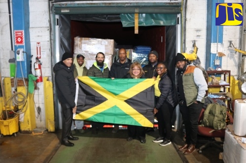 Jamaica’s Ambassador to the United States, His Excellency Major General (ret’d) Antony Anderson (left), President and Chief Executive Officer of EMD Sales International, Elda Devaré (fourth right), and volunteer, Natasha Forrest (second right), proudly display the Jamaican flag before the 40‑foot container of essential supplies bound for the island in support of Hurricane Melissa recovery efforts. Looking on are members of staff from the Embassy of Jamaica and EMD Sales at the company’s Baltimore warehouse in Maryland.