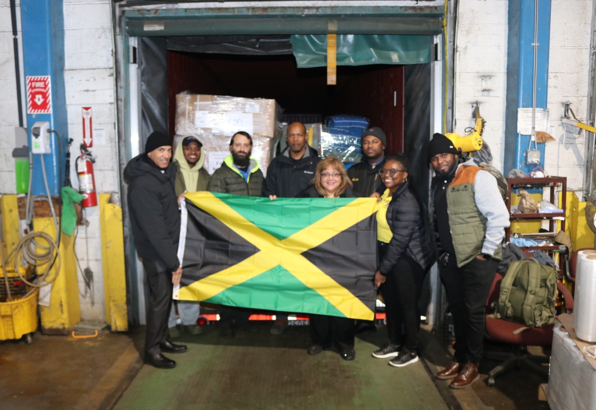 Jamaica’s Ambassador to the United States (US), His Excellency Major General (Ret’d) Antony Anderson (left), is joined by President and Chief Executive Officer (CEO) of EMD Sales, Elda Devaré (fourth right) and volunteer Natasha Forrest second right) in displaying the Jamaican flag in front of a 40-foot container packed with essential supplies bound for Jamaica, at the EMD Sales warehouse in Baltimore, Maryland, on December 11. Looking on are members of staff from the Embassy of Jamaica and EMD Sales.

