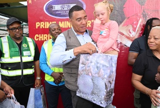 Prime Minister, Dr. the Most Hon. Andrew Holness, gives a gift to a child during a Christmas treat held at the Petersfield High School in Westmoreland on December 13. Also present was Minister of Labour and Social Security, Hon. Pearnel Charles Jr. (background, second left).

