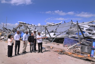 Minister of Water, Environment and Climate Change, Hon. Matthew Samuda (third from right), looks on as Agriculture, Fisheries and Mining Minister and Member of Parliament for St. Elizabeth South Western, Hon. Floyd Green (right), points to the destruction of the Black River Market in St. Elizabeth caused by Hurricane Melissa. Occasion was a tour of the area on Thursday (December 18), by a delegation from the Fund for Responding to Loss and Damage (FRLD). From left are Programme Manager for Programming and Country Engagement (PACE) at the Fund, Jihyea Kim;  Permanent Secretary in the Ministry of Water, Environment and Climate Change, Wayne Robertson; Executive Director of the FRLD, Ibrahima Cheikh Diong; and Acting Principal Director in the Climate Change Branch, Omar Alcock. 

