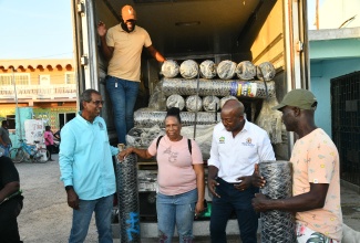 Minister of Labour and Social Security, Hon. Pearnel Charles Jr. (second right), offers words of encouragement to fishers affected by Hurricane Melissa, Annmaureen Spence (second left) and Carlton Thompson (right), during the handover of wire mesh on Friday (December 12) in Rocky Point, Clarendon. Sharing in the moment is Chief Executive Officer, National Fisheries Authority, Dr. Gavin Bellamy. 

