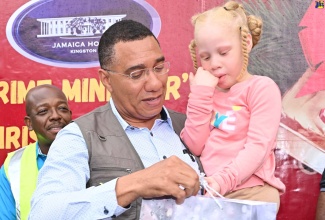 Prime Minister, Dr. the Most Hon. Andrew Holness gives a gift to a child, during a Christmas treat held at the Petersfield High School in Westmoreland on December 13. Also participating is Minister of Labour and Social Security, Hon. Pearnel Charles Jr (background, left).