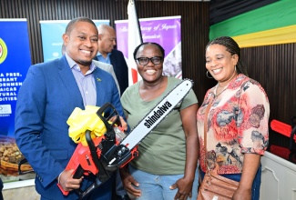Minister of Agriculture, Fisheries and Mining, Hon. Floyd Green (left), shares a photo opportunity with coffee farmer Miriam McDonald (centre) and Bernice Barrett (right), while holding one of the professional-grade chainsaws during the handover of power equipment to farmers affected by Hurricane Melissa, at the Jamaica Commodities Regulation Authority (JACRA), 1 Willie Henry Drive, off Marcus Garvey Drive in Kingston, on January 21. The equipment was provided through a United Nations Industrial Development Organization (UNIDO) project, funded by the Government of Japan.

