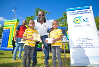 Minister Without Portfolio in the Office of the Prime Minister responsible for Science, Technology and Special Projects, Dr. the Hon. Andrew Wheatley, shares a photo opportunity with twins, Quaresiano (left) and Quaresma Nelson after presenting them with gifts. Occasion was the Kiddies Treat segment of the Urban Development Corporation