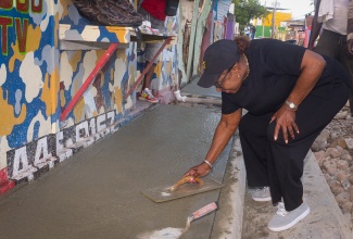 Minister of Culture, Gender, Entertainment and Sport, Hon. Olivia Grange, tries her hand at sidewalk paving along Cumberland Road during a tour of roads being upgraded under the Shared Prosperity through Accelerated Improvement to our Road Network (SPARK) Programme on Friday (January 9).

