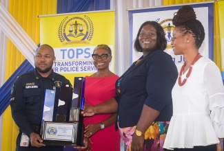 State Minister in the Ministry of National Security & Peace, Hon. Juliet Cuthbert Flynn (second left), presents the trophy for the top station in Area 5 to Brown’s Hall Station Commander, Sergeant Natoya Mighty (second right) and her colleague, Constable Kevaughnie Nelson.  Observing at right is Police Civilian Oversight Authority (PCOA) member, Vivette Miller. The trophy was among several awards presented at the annual Transforming Our Police Service (TOPS) Competition awards ceremony for 2025, held at the National Police College in Twickenham Park, St. Catherine, on Thursday (December 18).

