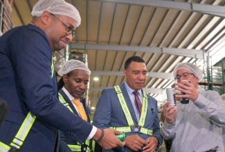 Prime Minister, Dr. the Most Hon. Andrew Holness (centre), looks at the contents of one of Wisynco Group Limited’s beer products being pointed out by the company