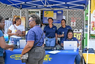 Jamaica Urban Transit Company (JUTC) Marketing Assistant, Nicole McDonald (standing in forefront), engages with a commuter during the JUTC SmartFare card activation drive held in Morant Bay, St. Thomas, on Saturday (February 7). Looking on in the background are revenue agents from the JUTC.