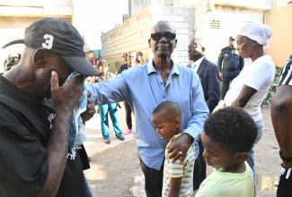 Minister of Local Government and Community Development, and Member of Parliament for West Kingston, Hon. Desmond McKenzie (centre), offers comfort to Jayce Pinnock