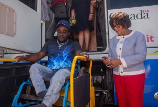 State Minister in the Ministry of Justice and Constitutional Affairs, Hon. Marisa Dalrymple-Philibert (right), operates the hydraulic lift on a mobile legal aid bus, to assist Leco Bradford, who utilises a wheelchair, to enter the unit. The event was the Legal Aid Council