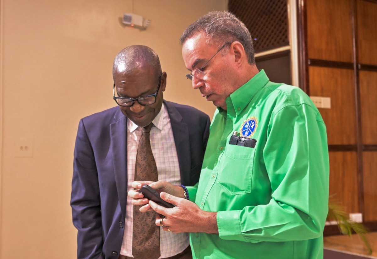 Minister of Energy, Transport and Telecommunications, Hon. Daryl Vaz (right), shares content on his smartphone with Director General, Office of Utilities Regulation (OUR), Ansord Hewitt, during a press conference at the PCJ Building in New Kingston on December 16, 2025.

