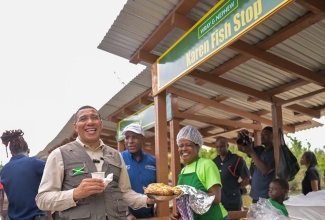 Prime Minister, Dr. the Most Hon. Andrew Holness (left), laughs as he is presented with a large container of fried fish by a vendor at the reopening of shops in Border, St. Elizabeth on January 16. Sharing in the moment is Minister of Industry, Investment and Commerce, Senator the Hon. Aubyn Hill.