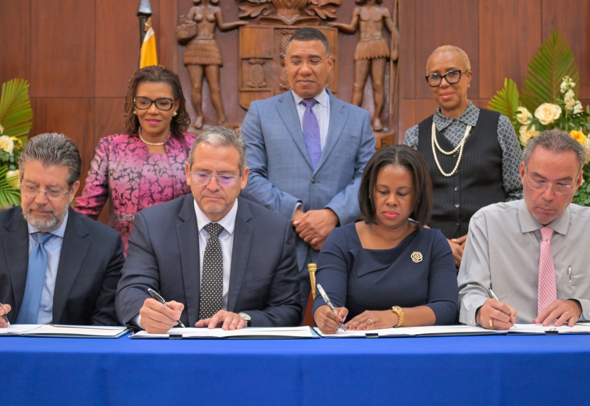 Prime Minister, Dr. the Most Hon. Andrew Holness (standing, centre), observes as (from left, seated) Chief Operating Officer, Trans Americas Fiber System, Jose Luis Rivera; Chief Executive Officer, Trans Americas Fiber System, Julio Bran; Permanent Secretary in the Ministry of Energy, Transport and Telecommunications, Kedesha Campbell Rochester, and Minister of Energy, Transportation and Telecommunications, Hon. Daryl Vaz, attach their signatures to documents during the letter of intent signing ceremony for the subsea cable project, at Jamaica House on February  3. Also observing the signing are Minister without Portfolio in the Office of the Prime Minister with responsibility for Efficiency, Innovation and Digital Transformation, Hon. Ambassador Audrey Marks (left), and Minister of Finance and the Public Service, Hon. Fayval Williams.

