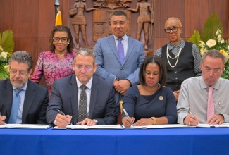 Prime Minister, Dr. the Most Hon. Andrew Holness (standing, centre), observes as (from left, seated) Chief Operating Officer, Trans Americas Fiber System, Jose Luis Rivera; Chief Executive Officer, Trans Americas Fiber System, Julio Bran; Permanent Secretary in the Ministry of Energy, Transport and Telecommunications, Kedesha Campbell Rochester, and Minister of Energy, Transportation and Telecommunications, Hon. Daryl Vaz, attach their signatures to documents during the letter of intent signing ceremony for the subsea cable project, at Jamaica House on February  3. Also observing the signing are Minister without Portfolio in the Office of the Prime Minister with responsibility for Efficiency, Innovation and Digital Transformation, Hon. Ambassador Audrey Marks (left), and Minister of Finance and the Public Service, Hon. Fayval Williams.

