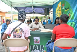 Rural Agricultural Development Authority (RADA) Data Entry Clerk, Wayne Breckenridge (centre), assists a farmer with the registration process for a Farmer Identification Card during Tuesday’s (March 10) RADA Connect event in Cedar Valley, St. Thomas. Beside him, RADA Telephone Operator, Latoya Burke, attends to another client.