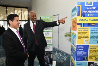 Director General of the Planning Institute of Jamaica (PIOJ), Dr. Wayne Henry (right), listens intently as International Population and Development Specialist, Dr. Jose Miguel Guzman (centre), makes a point about the PIOJ’s exhibition on Jamaica