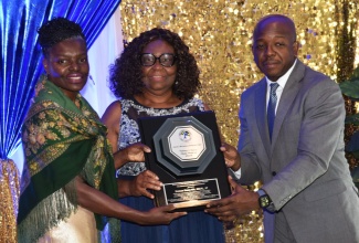 Minister of Labour and Social Security, Hon. Pearnel Charles Jr, joins President of the Jamaica Household Workers Union (JHWU), Elaine Duncan (left), in presenting the Lifetime Legacy Award for Advocacy and Empowerment to JHWU General Secretary, Shirley Pryce, at the organisation’s 35th anniversary gala & awards ceremony on Monday (March 16), at the Jamaica Pegasus hotel in New Kingston. 
 