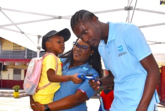 Director of Community Engagement at the HEART/NSTA Trust, Ronique Rhoden (left), and Mobile Robotics Trainee, Kristoff Rowe (right), introduces little Kayzia Edie to a robot, during a recent Youth Empowerment Fair hosted by the Social Development Commission (SDC) in the community.

