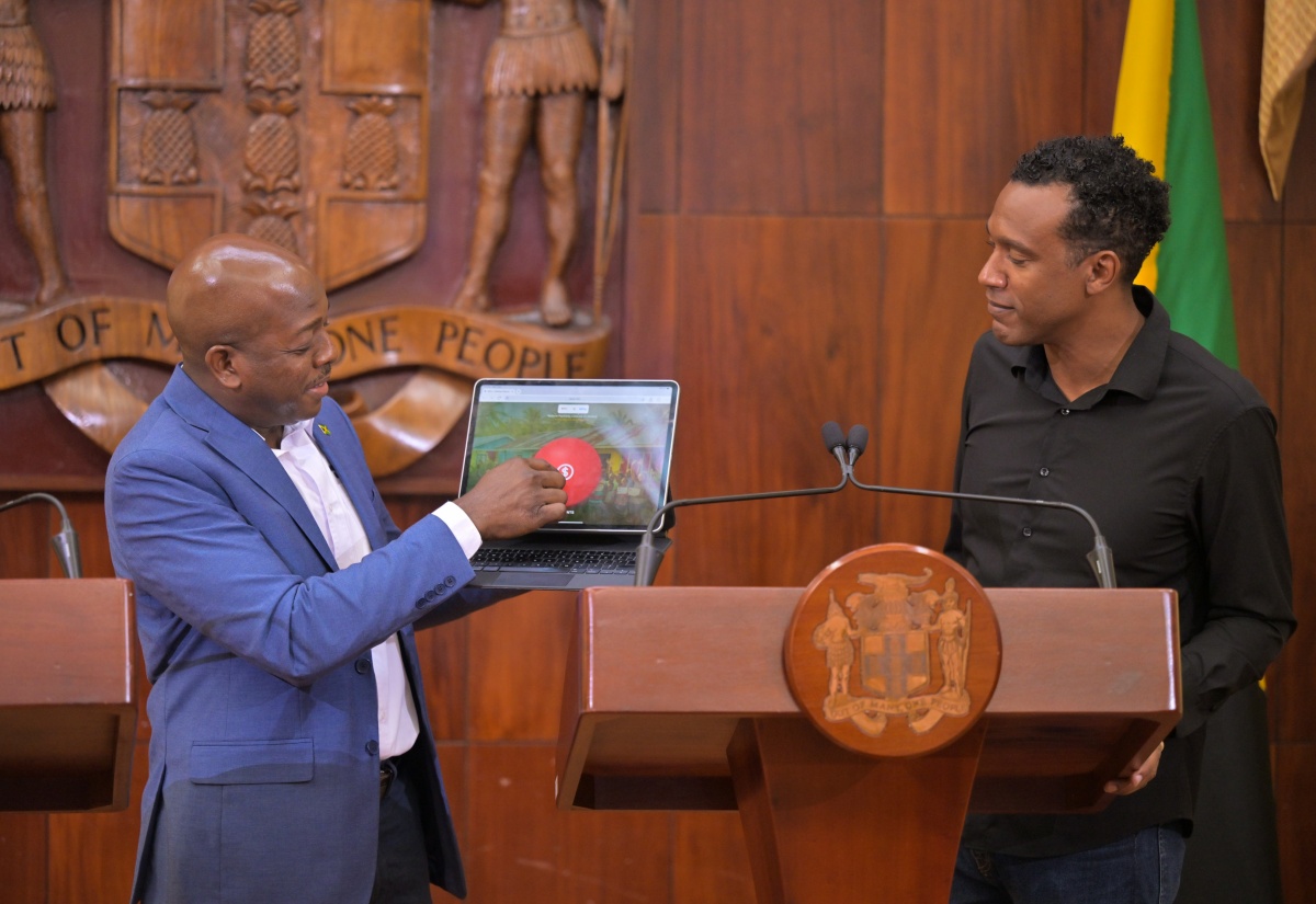 Minister of Labour and Social Security, Hon. Pearnel Charles Jr. (left), transmits notification messages to recipients under the Restoration of Owner or Occupant Family Shelters (ROOFS) initiative during Wednesday’s (March 11) Post‑Cabinet Press Briefing at Jamaica House. Looking on is Chief Marketing Officer and Country Manager at WiPay Jamaica, Kibwe McGann.

