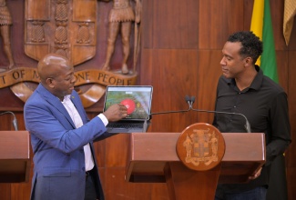Minister of Labour and Social Security, Hon. Pearnel Charles Jr. (left), transmits notification messages to recipients under the Restoration of Owner or Occupant Family Shelters (ROOFS) initiative during Wednesday’s (March 11) Post‑Cabinet Press Briefing at Jamaica House. Looking on is Chief Marketing Officer and Country Manager at WiPay Jamaica, Kibwe McGann.

