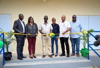 Minister of Local Government and Community Development, Hon. Desmond McKenzie (third left), and Mayor of Morant Bay, Councillor Louis Chin (third right), lead the ribbon-cutting to signify the opening of the St. Thomas Night Shelter on March 27. Joining them are (from left), Chief Executive Officer of the St Thomas Municipal Corporation, Kevin McIndoe; Member of Parliament for St. Thomas Eastern, Yvonne Shaw; Member of Parliament for St. Thomas Western, James Robertson,and Chairman of the Poor Relief Committee and Councillor for the Yallahs Division, John Lee.