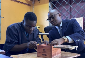 St. Lucia's Minister of Education with responsibility for Early Childhood Education, Special Needs, Continuing Education, Technical Education and Digital Transformation, Hon. Danny Butcher (right), observes a student living with special needs, Antwain Scott, work on a wooden gift box at Windsor School of Special Education in St. Catherine, on Wednesday (March 18).   

