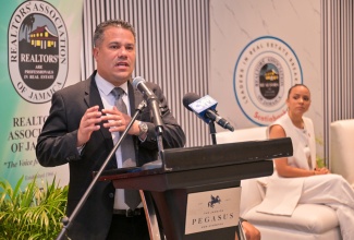 Minister of Water, Environment, and Climate Change, Hon. Matthew Samuda, delivers remarks as REALTORS® Association of Jamaica President, Gabrielle Gilpin‑Hudson, listens attentively. The occasion was the REALTORS® Association’s Leaders in Real Estate Breakfast, held at the Jamaica Pegasus Hotel in New Kingston on Thursday (February 26).