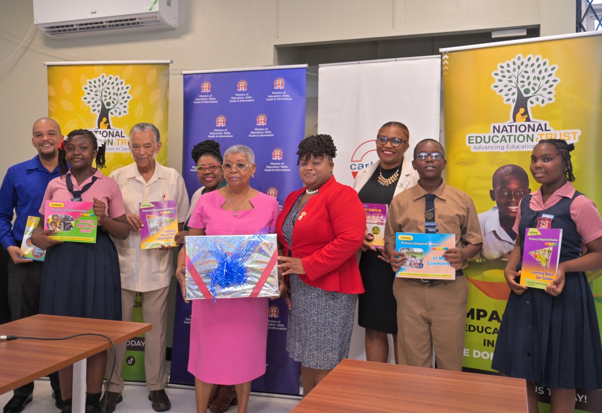 Carlong Publishers (Caribbean) Limited Chair, Shirley Carby (fifth left), presents a copy of one of the textbooks donated by the company for primary schools affected by Hurricane Melissa to Principal of Park Mountain Primary and Infant School in St. Elizabeth, Carlene Williams-Heath. Other participants (from left) are Carlong Publishers’ Chief Executive Officer, Jason Carby, and Director, Carl Carby; Assistant Chief Education Officer, Media Services Unit, Ministry of Education, Skills, Youth and Information, Dr. Nadine Simms; National Education Trust (NET) Executive Director, Latoya Harris-Ghartey; and students of Park Mountain Primary. The textbooks were officially presented during a formal handover ceremony on Thursday (March 12), at the Ministry’s Student Assessment Unit, Caenwood Centre, Kingston.

