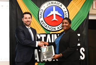 Acting Director General of the Jamaica Civil Aviation Authority (JCAA), Nichole Morgan, receives the findings of a Sustainable Aviation Fuel Feasibility Study from Sustainable Aviation Senior Manager at ICF Consulting, Yasar Yetiskin, at the handover exercise on Tuesday, April 14, at the JCAA’s Winchester Road headquarters in Kingston.  
