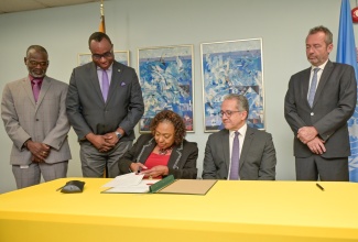 Minister of Culture, Gender, Entertainment and Sport, Hon. Olivia Grange (centre), affixes her signature to the Instrument of Ratification for the UNESCO 1970 Convention on the Means of Prohibiting and Preventing the Illicit Import, Export and Transfer of Ownership of Cultural Property on Thursday (April 2) at the Ministry in New Kingston. Looking on is United Nations Educational, Scientific and Cultural Organization (UNESCO) Director-General, Professor Khaled El-Enany (seated second right). Also observing (from second left) are Permanent Secretary in the Ministry, Denzil Thorpe; Permanent Secretary, Dean-Roy Bernard, and Regional Director and Representative of the UNESCO Regional Office for the Caribbean, Eric Falt (right).