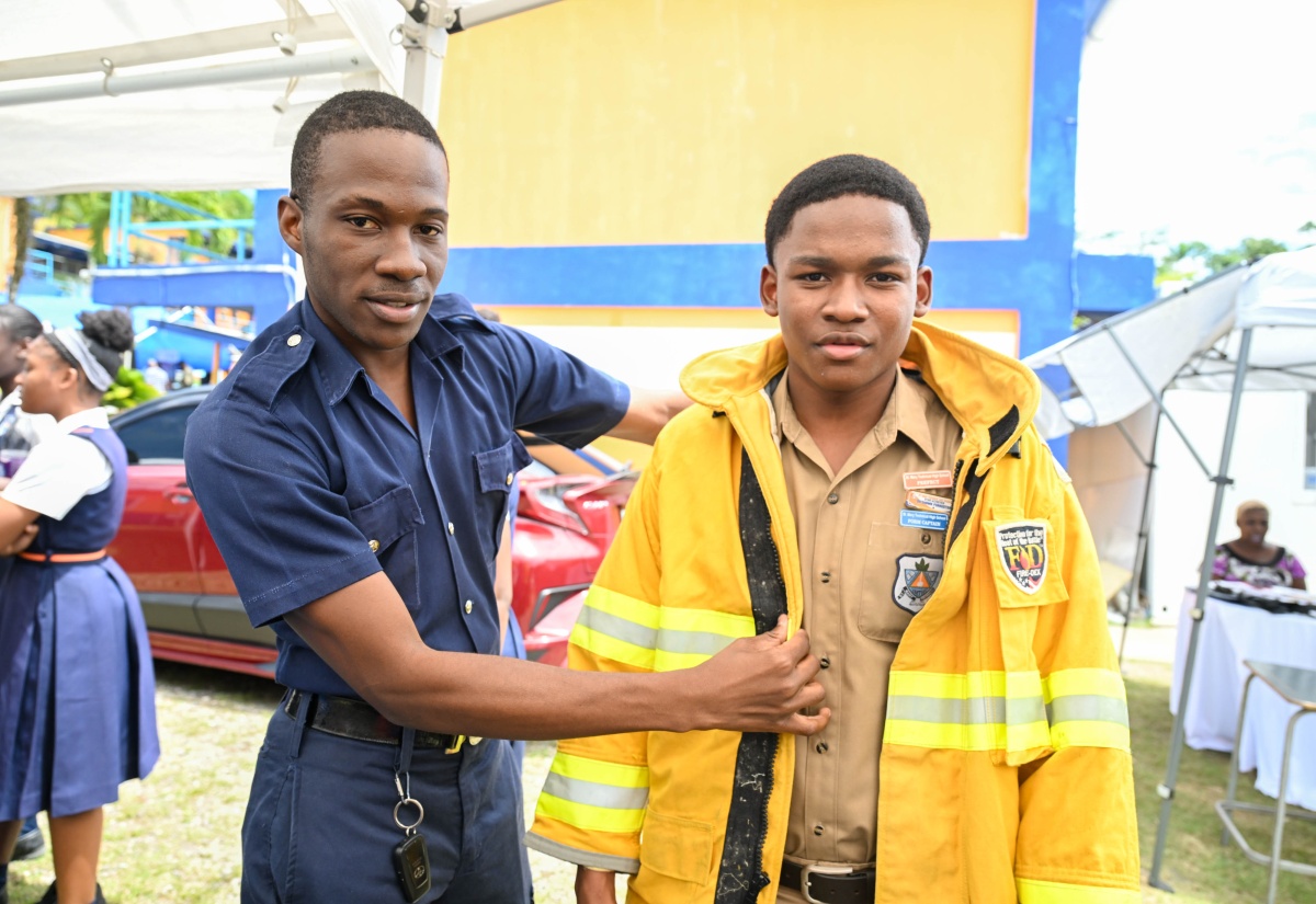 Kyron Parry (left) of the Jamaica Fire Brigade (JFB) Fire Safety Prevention and Investigation Branch shares a moment with St. Mary Technical High School student Dashawn Forrester, who tries on JFB gear during a Career Day expo at the institution on March 25. 
