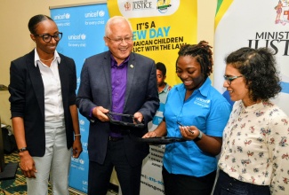 Minister of Justice and Constitutional Affairs, Hon. Delroy Chuck (second left), looks on as Technology for Development Officer at the United Nations Children's Fund (UNICEF), Sabrina Atkinson (second right), points out something of interest on one of the 20 tablets donated to the Child Diversion Branch in the Ministry by UNICEF. The devices were handed over during a digitisation and data management system training for members of the Branch held on March 27 at the Courtyard by Marriott in Kingston. Others (from left) are Director of the Branch, Venisa Clarke;  and Child Protection Specialist, UNICEF, Marjana Badas. 
