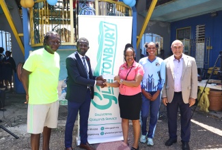 Custos Rotulorum of Trelawny, Hugh Gentles (right), who is General Manager of food distribution company Glastonbury, looks on as Shelly-Ann Bryan (centre) of Glastonbury hands over a cheque to Holland High School Principal, Dayle Evans (second left). The occasion was a ceremony held at the institution in Trelawny on (March 30) to celebrate the school