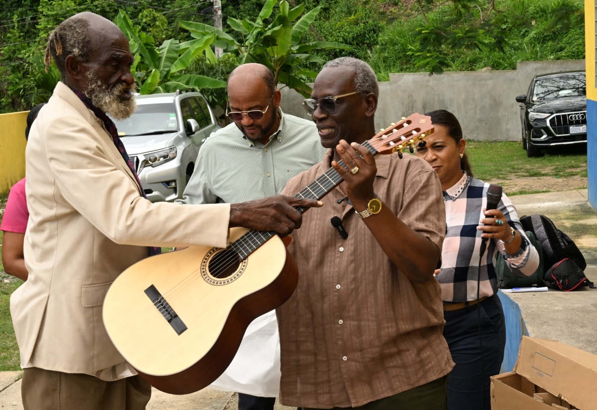 Minister of Local Government and Community Development, Hon. Desmond McKenzie (right), hands over a new guitar to musician and regular visitor to the St. Ann Drop-in Centre, Allmond Belnavis (left), during a visit to the facility in Ocho Rios, on Tuesday (April 7). Looking on are St. Ann