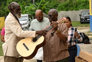 Minister of Local Government and Community Development, Hon. Desmond McKenzie (right), hands over a new guitar to musician and regular visitor to the St. Ann Drop-in Centre, Allmond Belnavis (left), during a visit to the facility in Ocho Rios, on Tuesday (April 7). Looking on are St. Ann