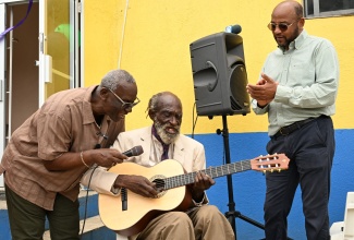 Minister of Local Government and Community Development, Hon. Desmond McKenzie (left), sings along with musician and regular visitor to the St. Ann Drop-in Centre in Ocho Rios, Allmond Belnavis (centre), after presenting him with a new guitar on April 7.  At right is St. Ann's Bay Mayor, Michael Belnavis.
