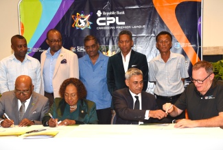 Tourism Minister, Hon. Edmund Bartlett (left, seated); Minister of Culture, Gender, Entertainment and Sport, Hon. Olivia Grange (second left, seated); Owner of the Jamaica Kingsmen Caribbean Premier Leage (CPL) T20 Cricket Franchise, Fawad Sarwar (second right, seated); and CPL Chief Executive Officer (CEO), Pete Russell (right, seated), sign documents during a press conference at the Jamaica Pegasus Hotel in New Kingston on Tuesday (March 31) to announce the new franchise. Looking on (from left, standing) are: Mayor of Kingston, Councillor Andrew Swaby; Tourism Director, Donovan White; Chief Medical Officer for Cricket West Indies (CWI) and the CPL, Dr. Akshai Mansingh; CWI CEO, Chris Dehring; and Jamaica Cricket Association (JCA) President, Dr. Donovan Bennett.