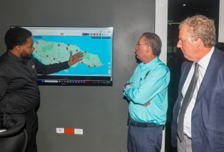 Energy, Transport and Telecommunications Minister, Hon. Daryl Vaz (centre), looks on while  Elhydro operations manager, Sanjay Brown (left), points out features of a digital map used in monitoring the operations of the National Rural School Bus Programme. Occasion was the launch of the new School Bus Operations Centre (SBOC) at 26 Lyndhurst Road in Kingston on Wednesday (April 15). Also observing is Chargé d’Affaires, United States Embassy, Scott Renner.