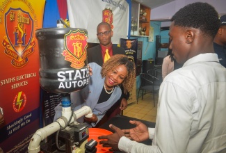 Minister of Education, Skills, Youth and Information, Senator Dr. the Hon. Dana Morris Dixon (left), tries out an automatic chicken feeder made by students of St. Andrew Technical High School, during an alumni engagement visit on Tuesday (April 14), in commemoration of the institution’s 65th anniversary. Also pictured is Principal, Dr. Worrel Hibbert..
