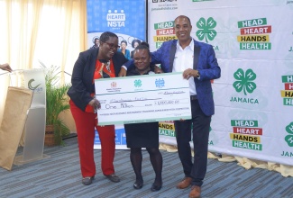 Executive Director of the Jamaica 4-H Clubs, Peter Thompson (right) and Manager of Entrepreneurial Skills Development at the HEART NSTA/Trust, Stacy Mignott, present the first place prize of $1 million in the Rural Youth Economic Empowerment Programme (RYEEP) National Agribusiness Pitch Competition, to Marshana Furze from Westmoreland. Occasion was the finals of the competition held at the Cardiff Hotel in Runaway Bay, St. Ann on Thursday, May 21.