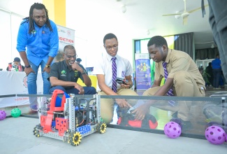 Permanent Secretary in the Ministry of Culture, Gender, Entertainment and Sport, Denzil Thorpe (second left), and Director of the Male Empowerment Unit at the Bureau of Gender Affairs, Nashan Miller (left), observe as Kingston College programmers, Samuel Francis (second right) and Iveco Bryan, demonstrate their autonomous robot. The occasion was Friday