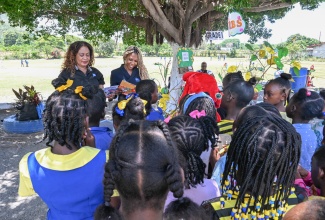 Acting Community Relations Officer-Eastern at the National Water Commission (NWC), Marlene Davis (left) and Customer Care Officer, NWC St. Thomas, Shenae Gordon-Walker, read to students at the Yallahs Primary School on Read Across Jamaica Day on Tuesday (May 5).
